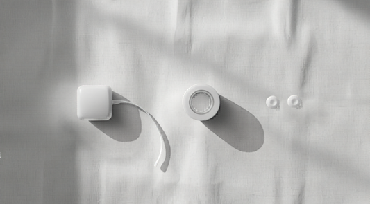 Black and white editorial flat lay showing a sticky bra, a roll of boob tape and silicone nipple covers on linen, classic monochrome lifestyle styling.