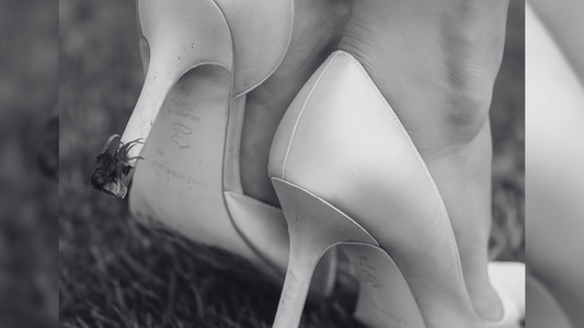Close-up of a pair of ivory high heels on a grassy lawn, with the heels slightly sinking into the grass due to lack of heel protectors, illustrating the need for heel protection accessories