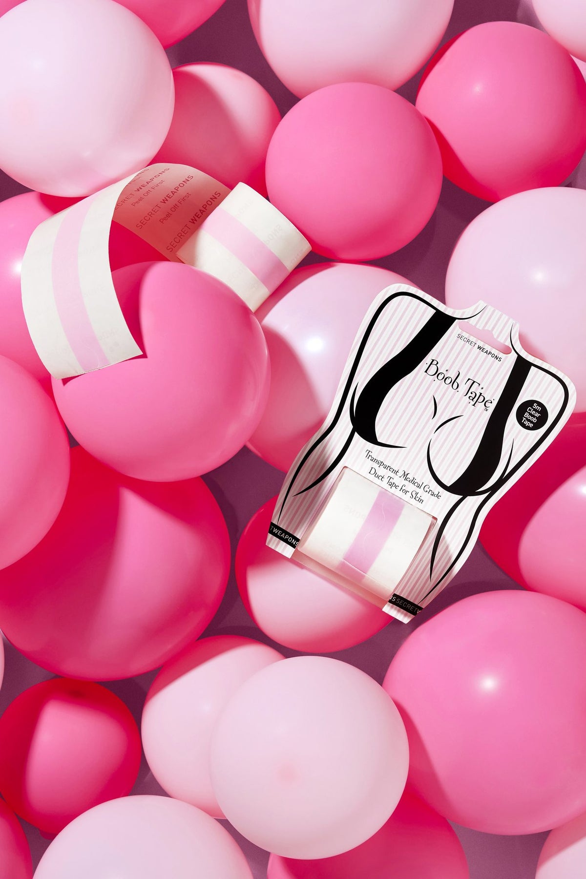 A packaging of Clear Boob Tape with the roll sitting amongst dark pink and light pink balloons.