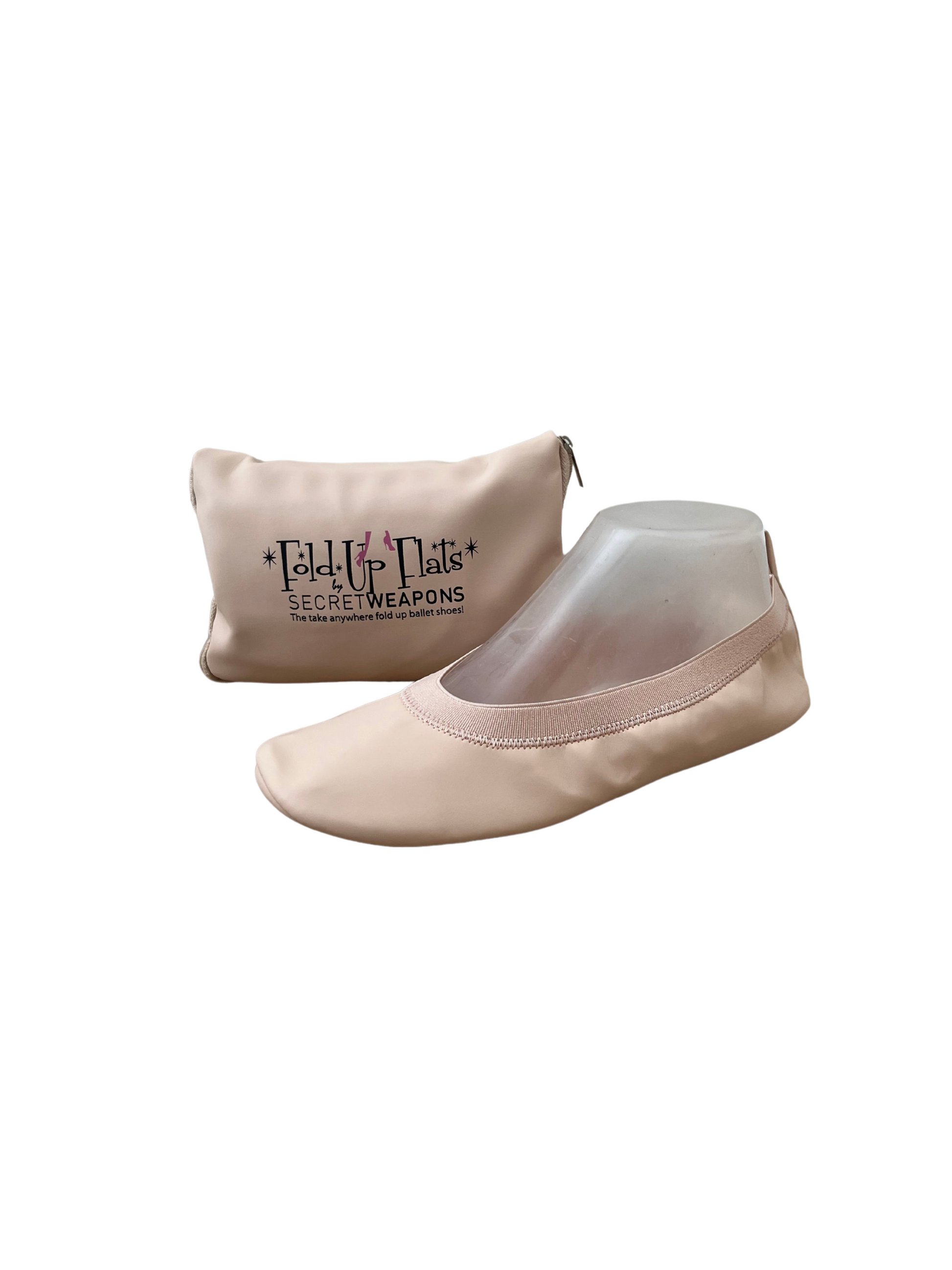 Nude colour foldable ballet flat sitting in front of a carry purse on a white background
