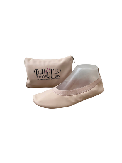 Nude colour foldable ballet flat sitting in front of a carry purse on a white background