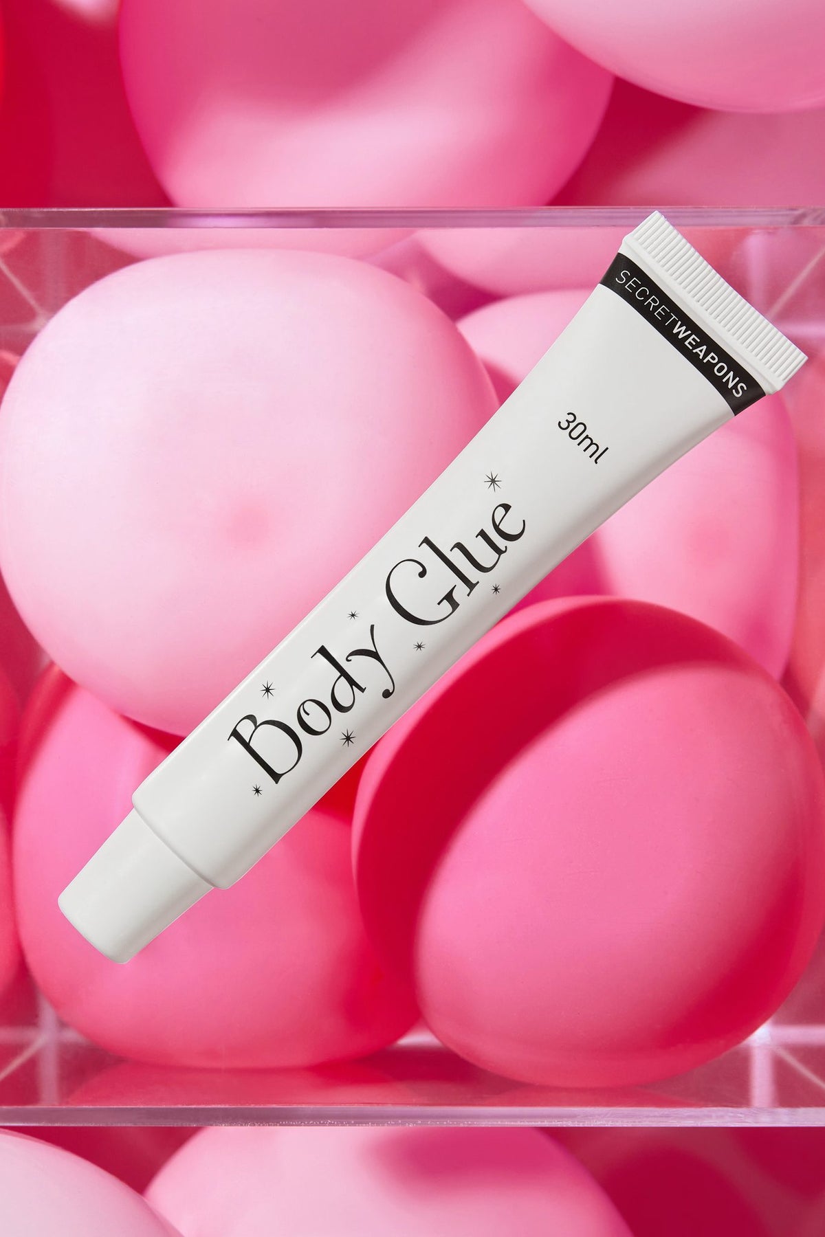 Body Glue 30 ml available in tube packaging against a transparent container floating on pink ballons