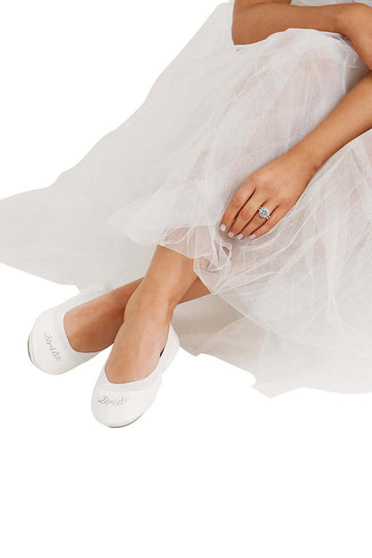A model wearing a wedding gown and White Bride ballet flats with the BRIDE embellished letters showing on the shoes