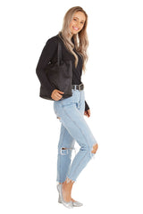 A woman smiling wearing blue jeans, a black shirt and silver fold up ballets on her feet. The woman has the ballet flats carry bag on her shoulder against a white background. 
