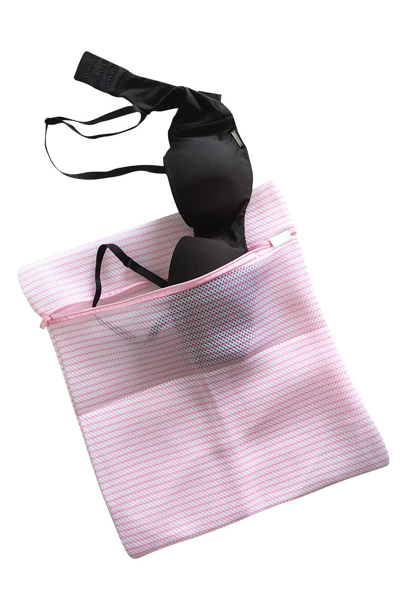 A black bra is partially inside a pink mesh zipper laundry bag, placed against a plain white background.