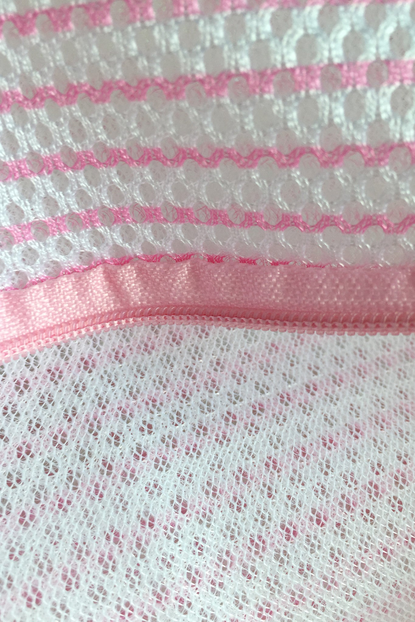 A close-up of pink and white mesh fabric, featuring stripes and textures with circular patterns, likely part of a garment or accessory, highlighting the intricate design and stitching details.