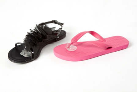 A black sandal and a pink flip-flop are resting side by side on a white background. The sandal features decorative ruffles, while the flip-flop has a simple thong design.Toe Protectors are applied to the both the black sandal and pink flip flop.