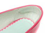 A close-up view of a pink shoe's interior shows a scalloped blue insole, with a smooth, light-colored lining in a clean, bright setting.